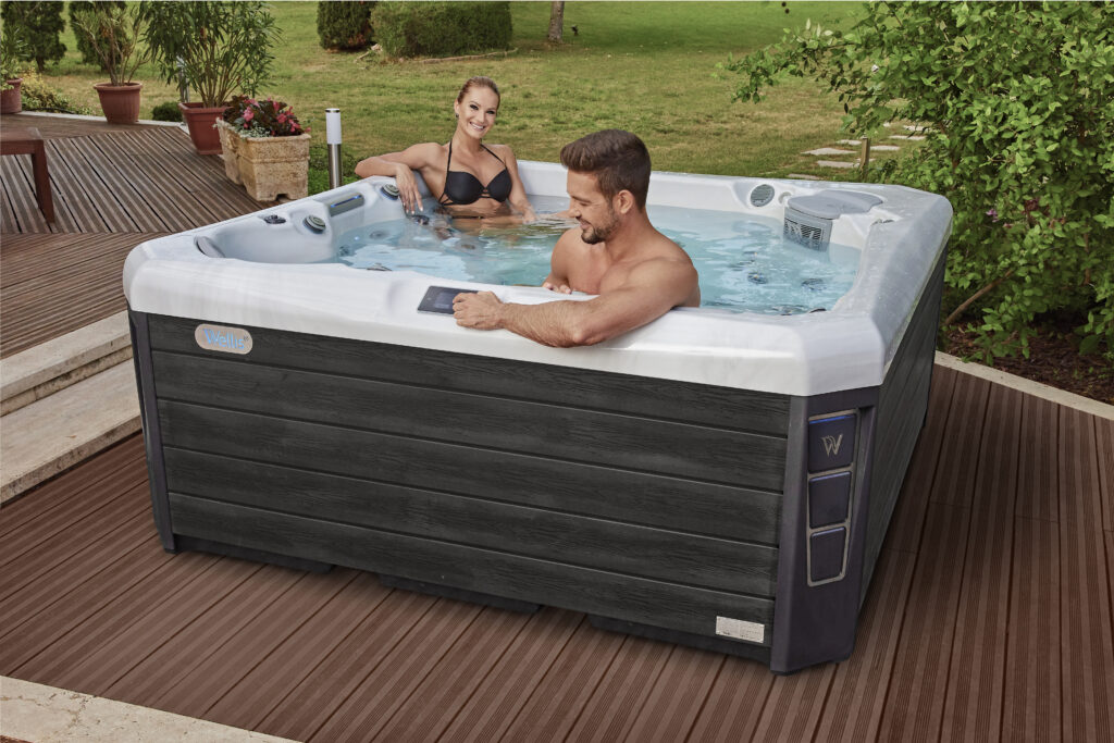 A couple sits in a hot tub as the man adjusts the settings to stay on top of wellness.