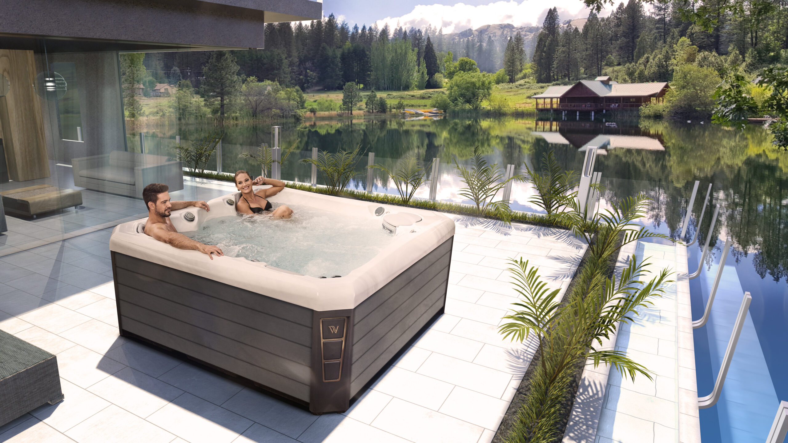 A couple takes time to relax in their Wellis spa that situated on a modern deck with plants overlooking a lake.