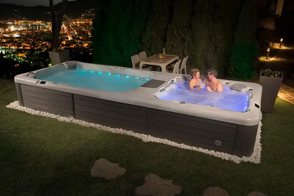 Picture of two people in an illuminated swim spa hot tub combo at night.